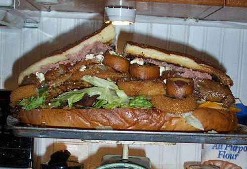 The 30,000 Calorie Sandwich Sandwich filled with ground beef, bacon, corn dogs, ham, pastrami, roast beef, bratwurst, braunschweiger and turkey, topped with fried mushrooms, onion rings, swiss/provolone/cheddar/feta/parmesan cheeses, lettuce and butter on a loaf white bread.  (submitted by Kai via nanbelegorn)